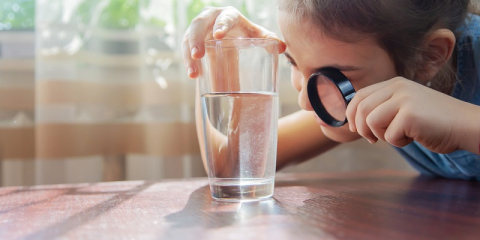 Jeune fille regardant un verre d'eau à la loupe